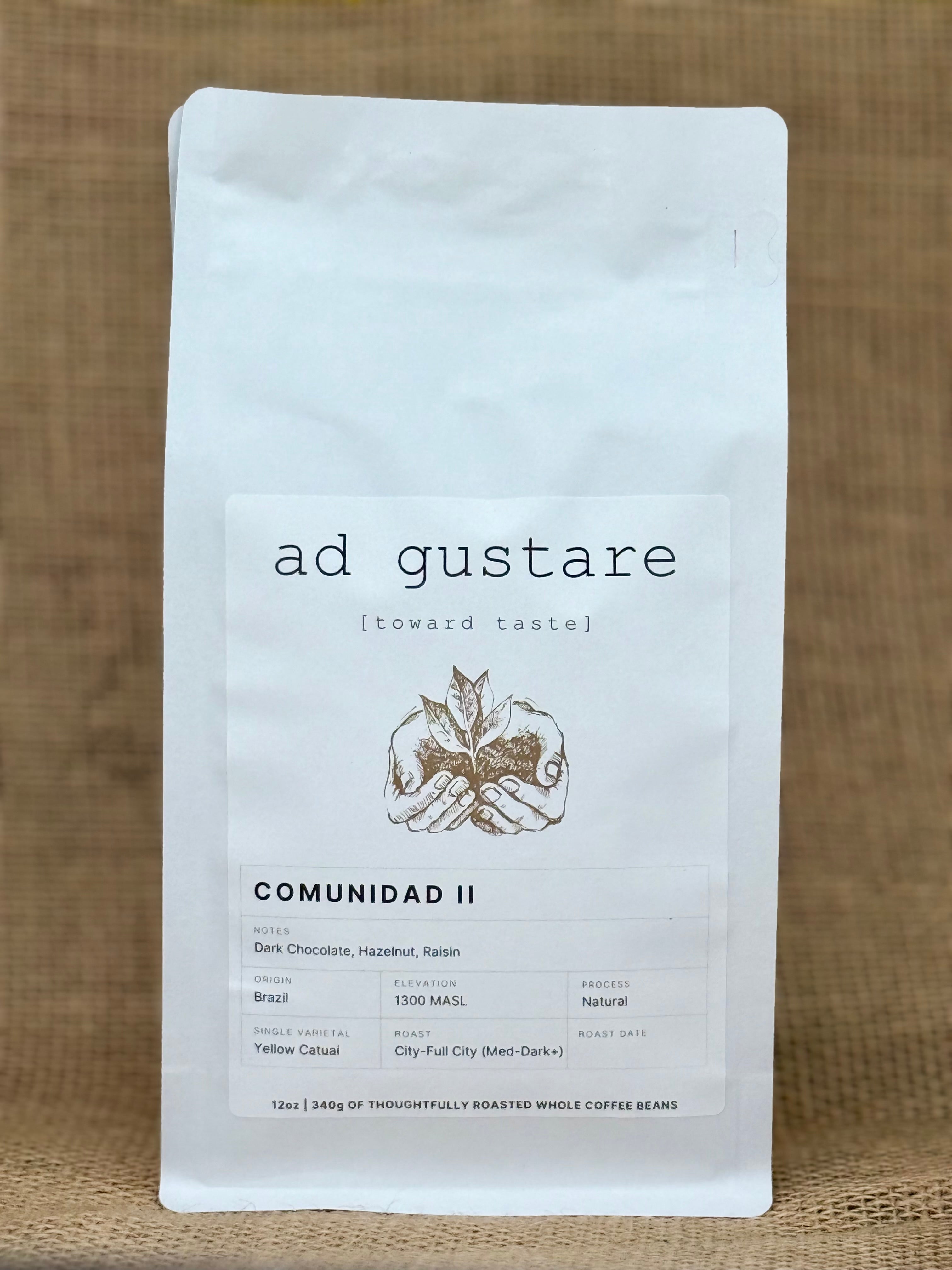 Ad Gustare Comunidad II Brazil coffee bag with minimalist white label featuring hands holding coffee plant illustration, photographed on burlap.