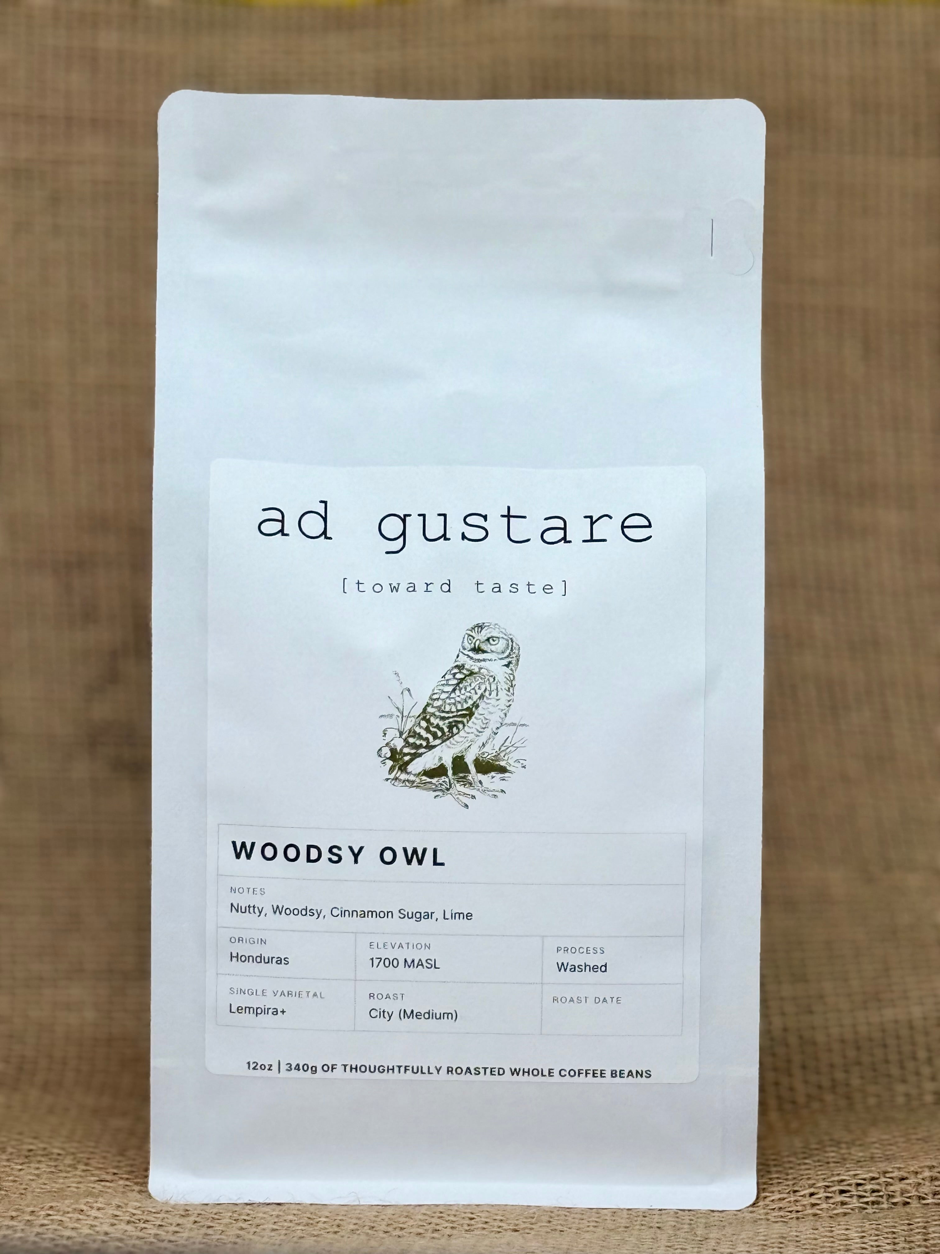 Ad Gustare Woodsy Owl Honduras coffee bag with minimalist white label featuring an illustrated owl, photographed on burlap. Front view