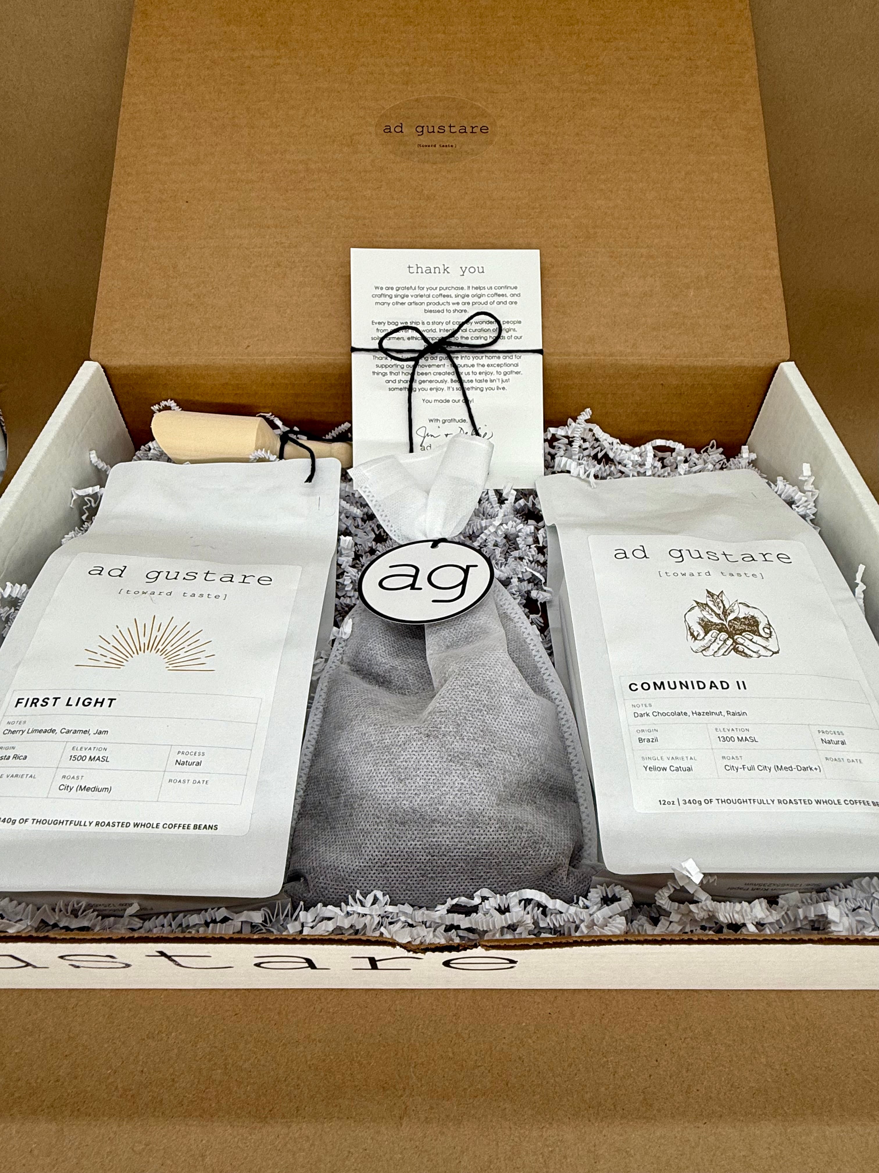 Ad Gustare AG 100 Coffee Club subscription box featuring two specialty coffee bags, branded accessories, and a thank you card arranged in a gift box. Front view